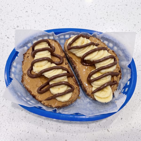 Two slices of toast topped with peanut butter, banana slices, and chocolate drizzle on a blue plate.