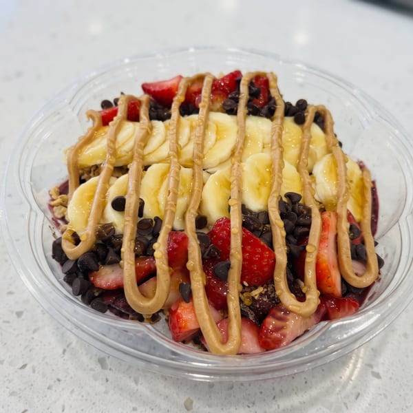Acai bowl with sliced bananas, strawberries, chocolate chips, and peanut butter drizzle in a clear bowl.