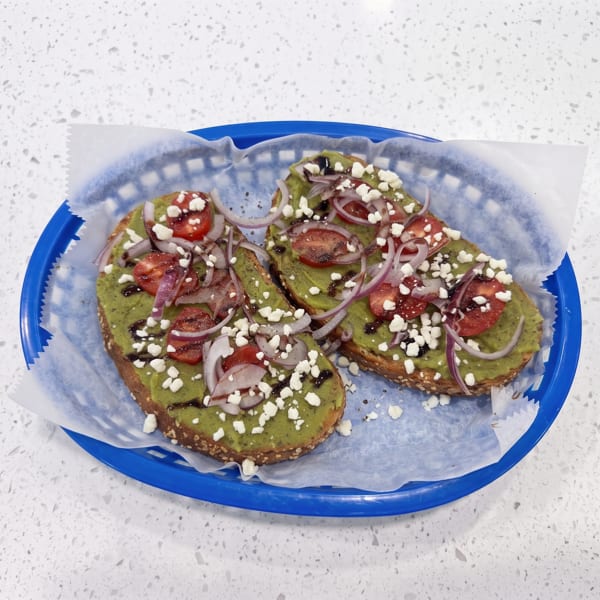 Three avocado toasts topped with tomatoes, red onions, feta cheese, and balsamic drizzle on a blue plate.