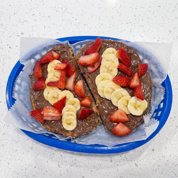 Two slices of chocolate-spread toast topped with sliced strawberries and bananas on a blue tray.