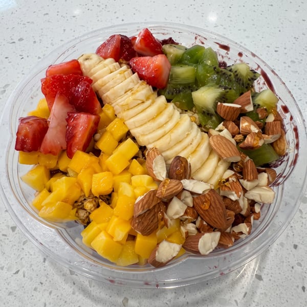 Colorful fruit bowl with strawberries, bananas, kiwi, mango, and almonds on a white speckled counter.